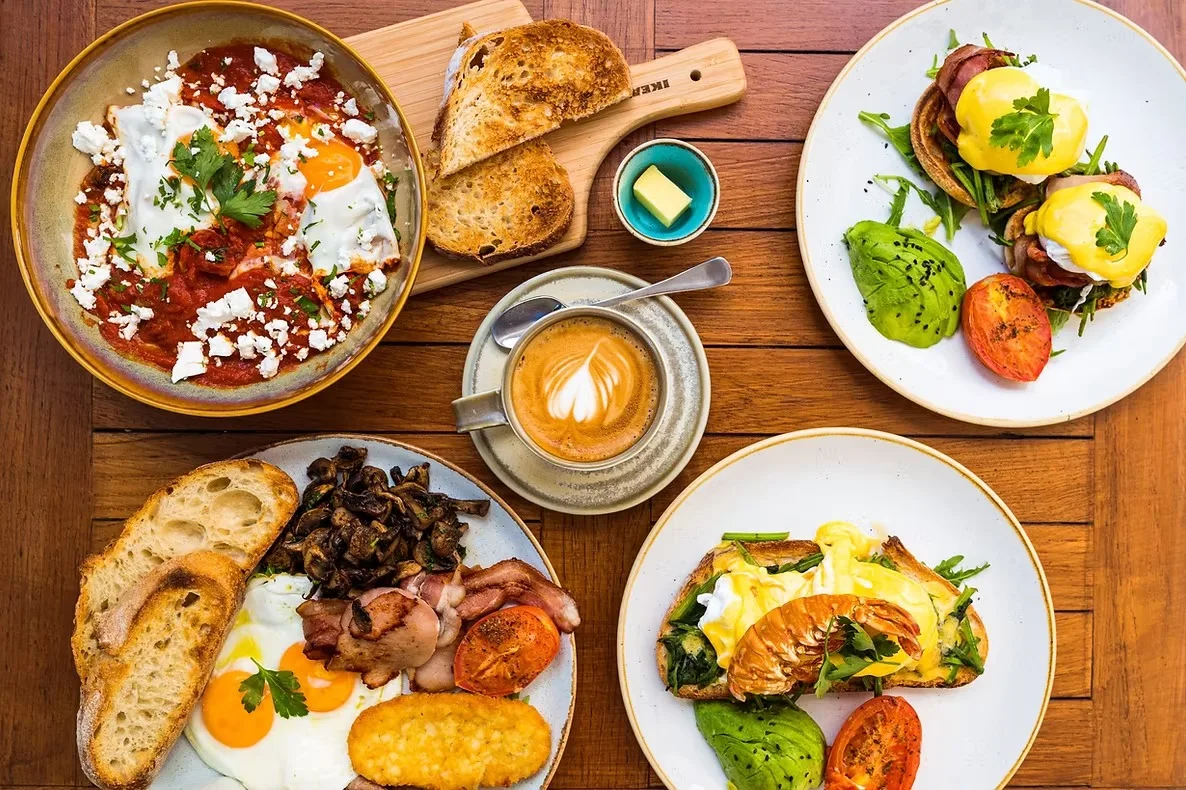 Brunch spread on a timber table at Soho on Miller: shakshuka, eggs benedict, a big breakfast, toast and a flat white