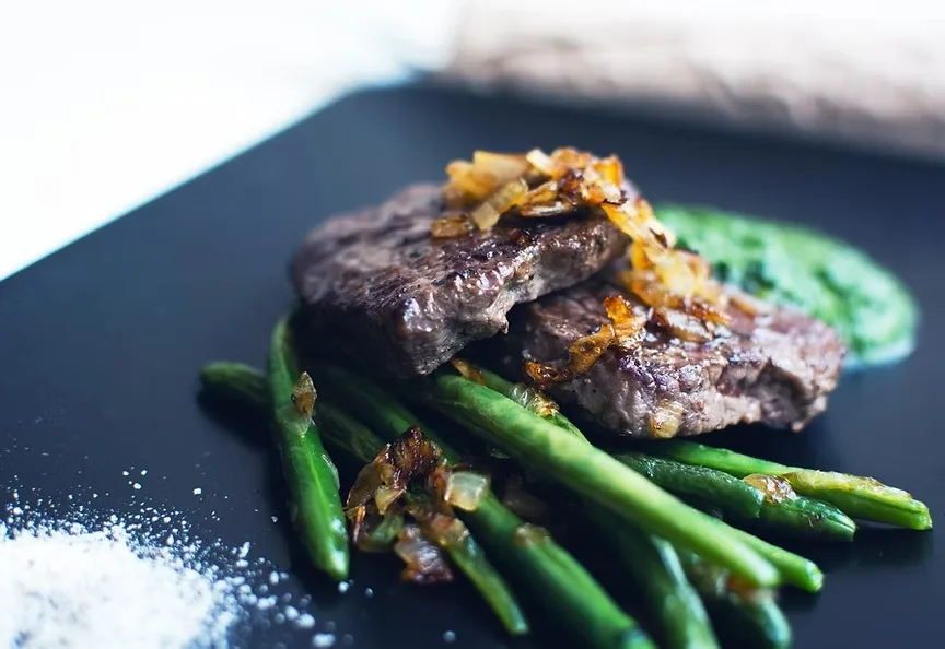 Grilled steak with asparagus and caramelised onions on a dark plate